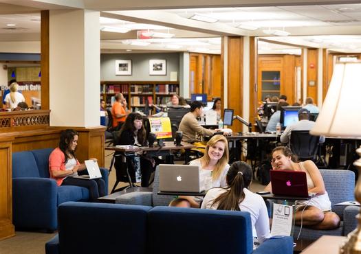 Students in library at computers and couches around lobby area.