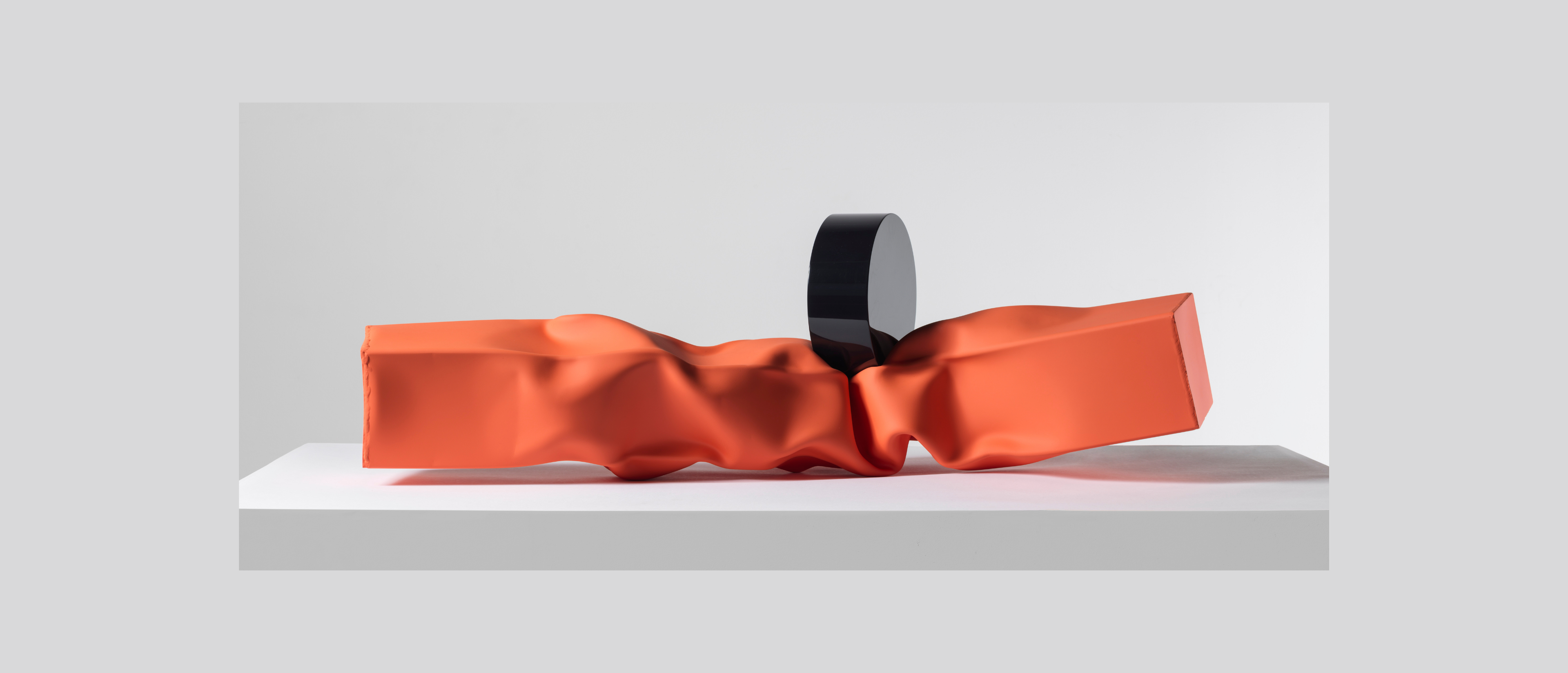 Black cylinder crushes a red metal beam on white surface.