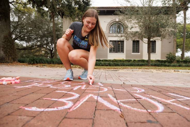 A student crafts a chalk-written note of kindness on the sidewalk at Rollins.