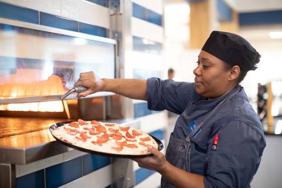 A campus chef puts a pizza into the oven.