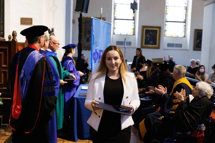A student carries a watch key, stole, and certificate that she received during a Phi Beta Kappa induction ceremony.