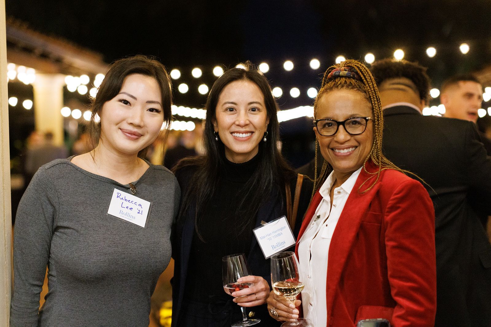 Three female alumni smiling at an evening holiday event.