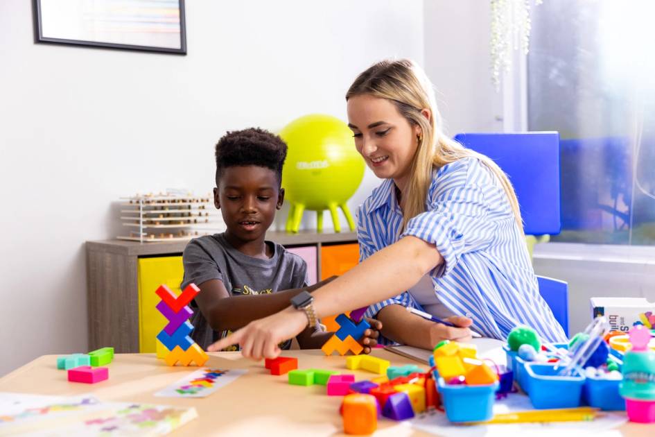 Adult and child building colorful block structures together at classroom table.