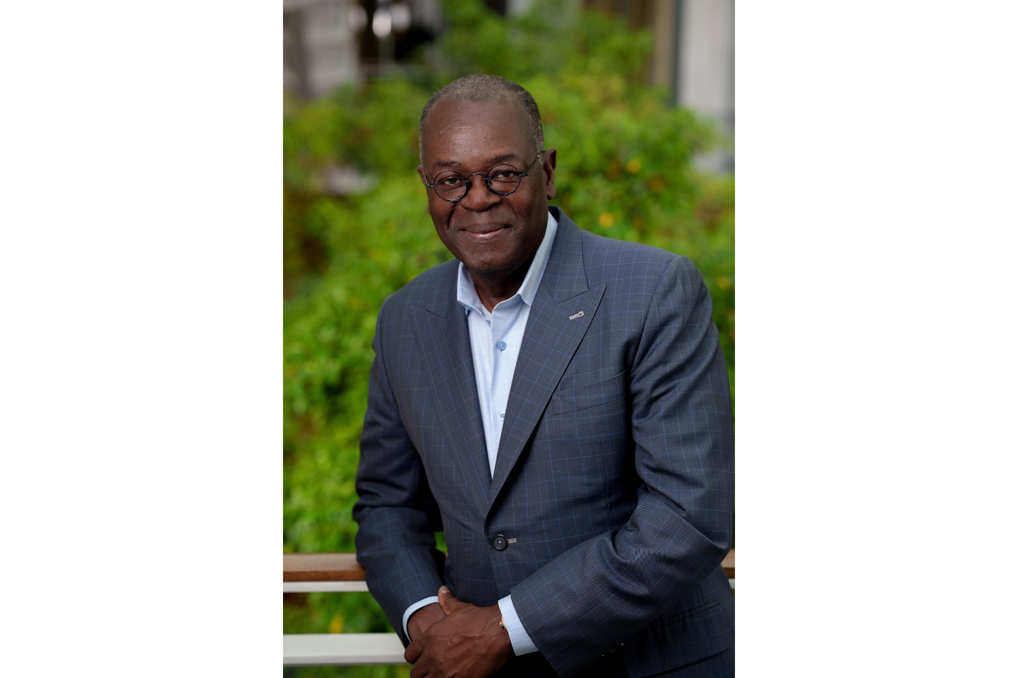 Portrait of Rollins alumnus and trustee Rodney C. Adkins ’81 standing outdoors with green foliage behind him.