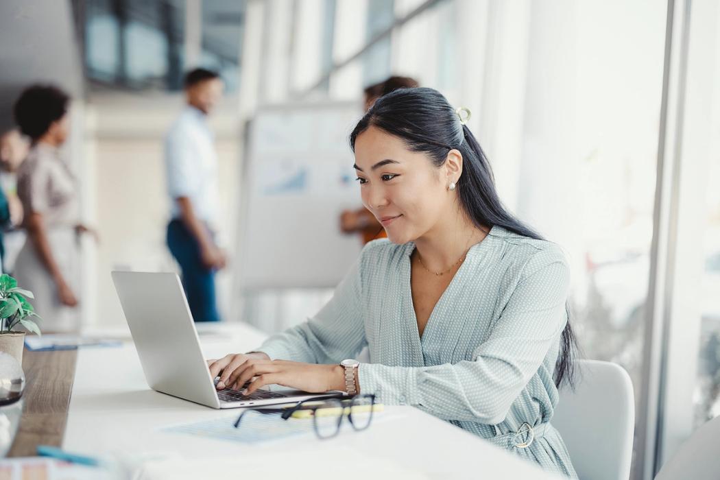 A communication professional works on her laptop in a sunlit office.