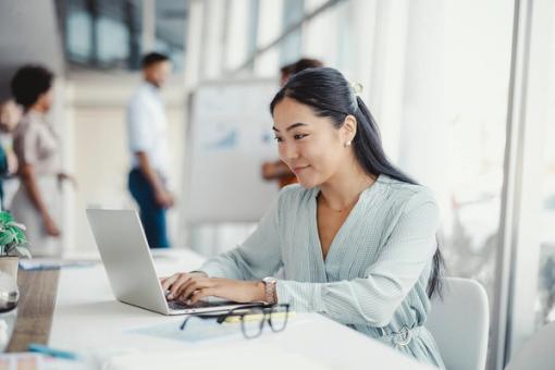 A communications professional works on her laptop in a sunny office building.