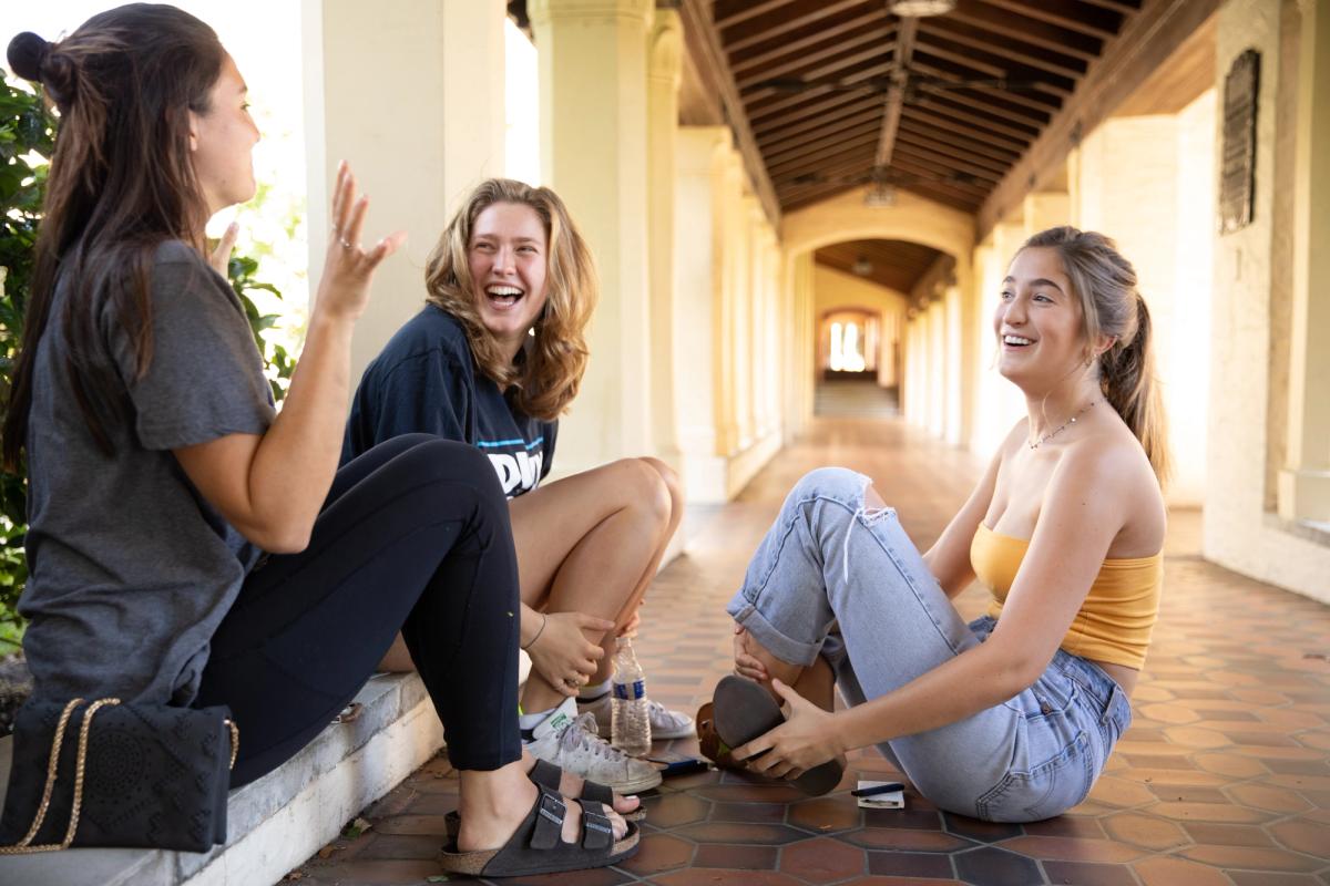 Three students laugh together while hanging out on campus.