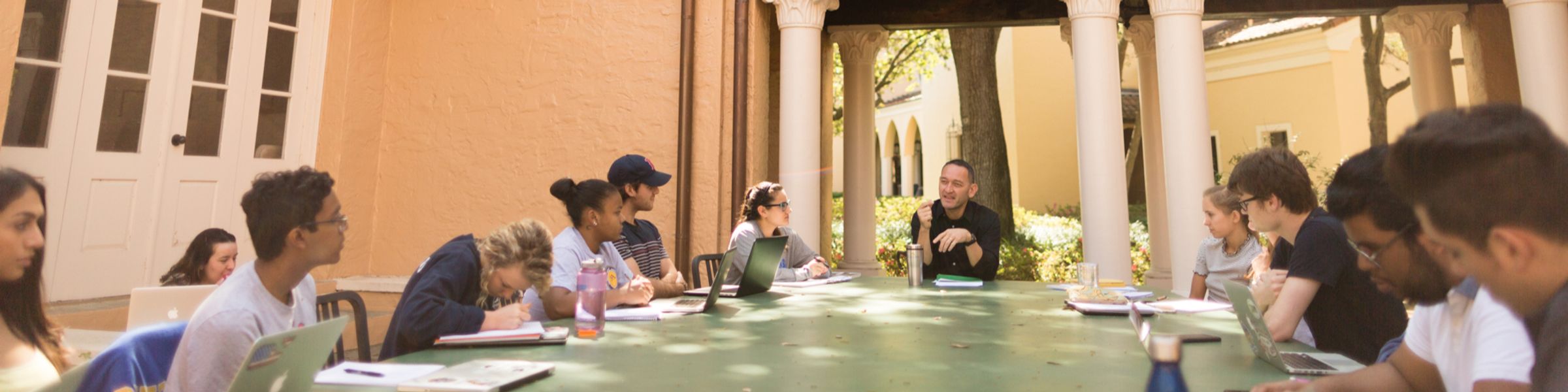 A political science professor leads a class discussion around an emerald table in Rollins’ Orlando Hall outdoor classroom.