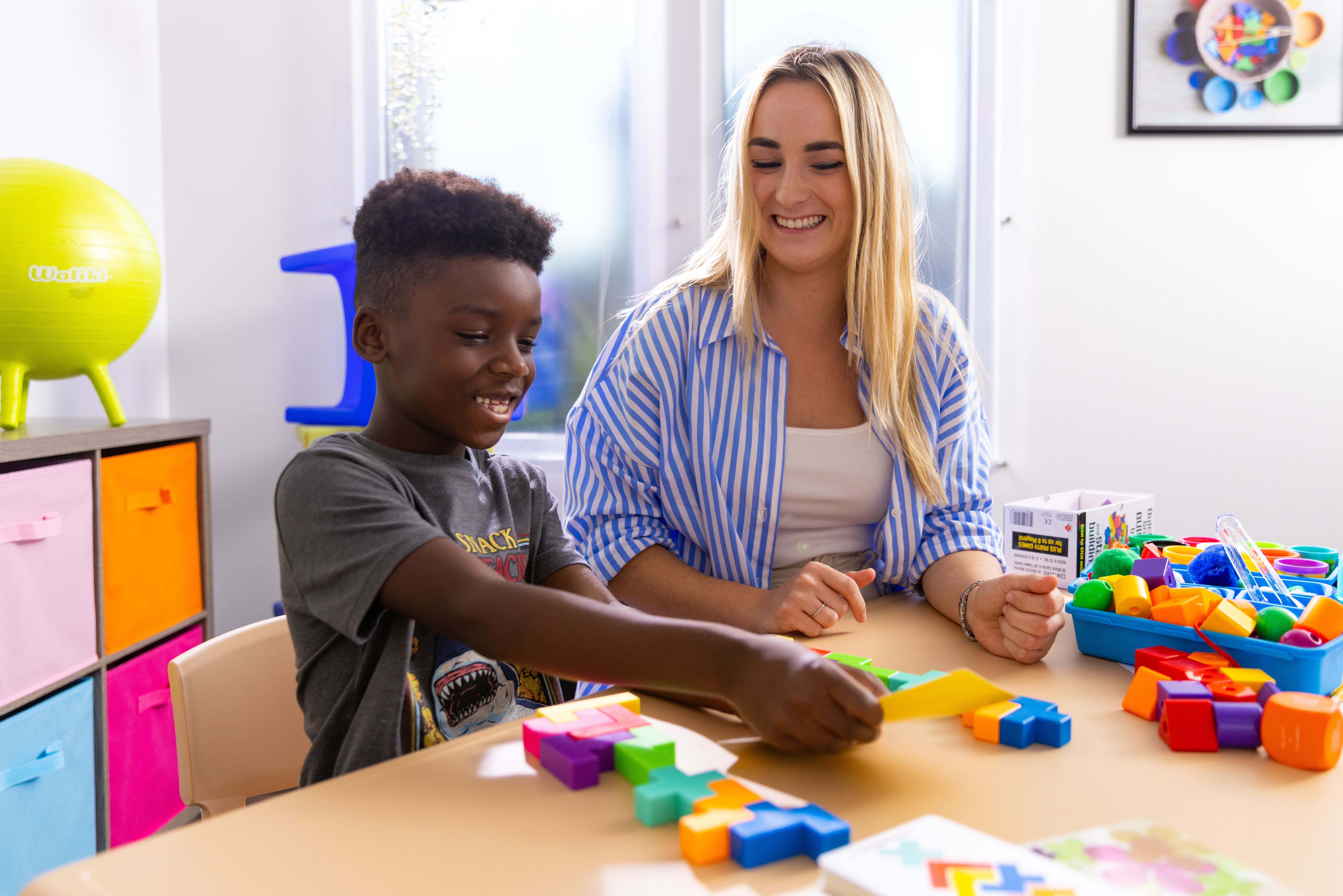 An applied behavior analyst observes a young patient stacking colorful blocks.