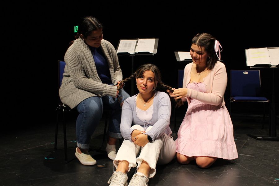 Two women are seated behind a third woman, braiding her hair into pigtails