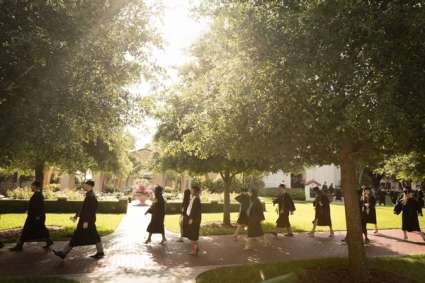 Students wearing caps and gowns walk to a commencement ceremony on Rollins College’s campus.