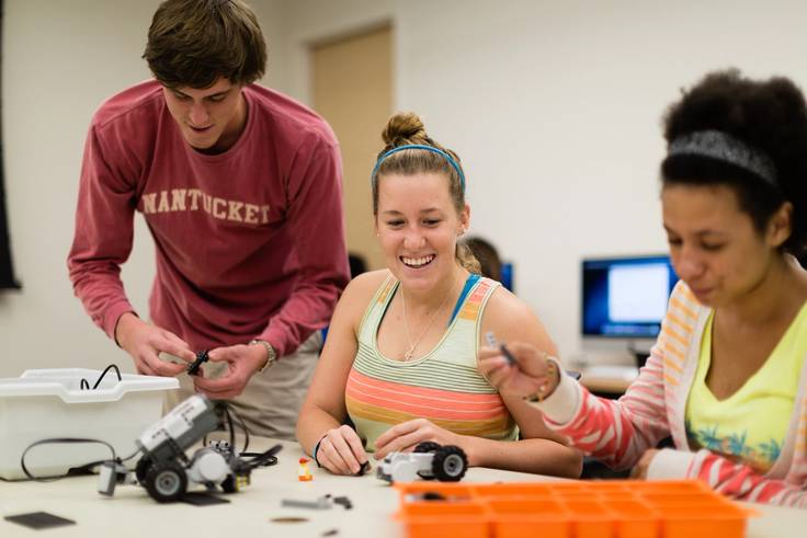 Three Rollins College students work on building a robot in class.