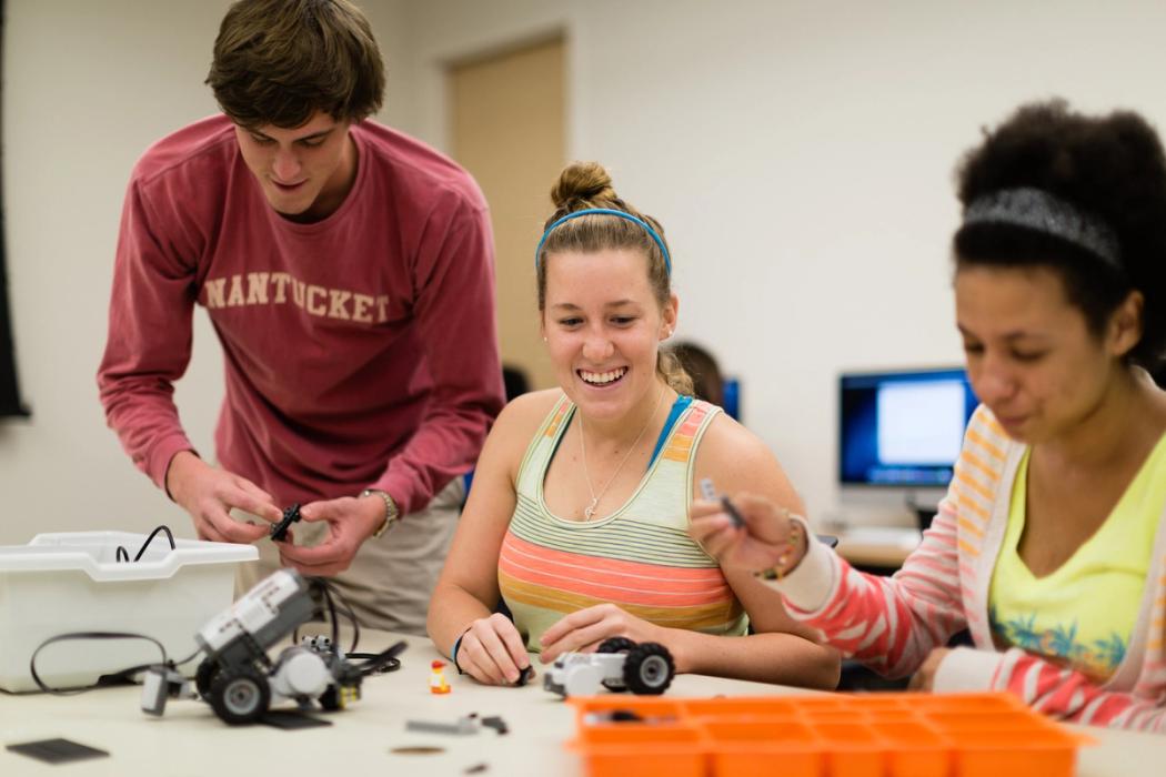 Three Rollins College students work on building a robot in class.