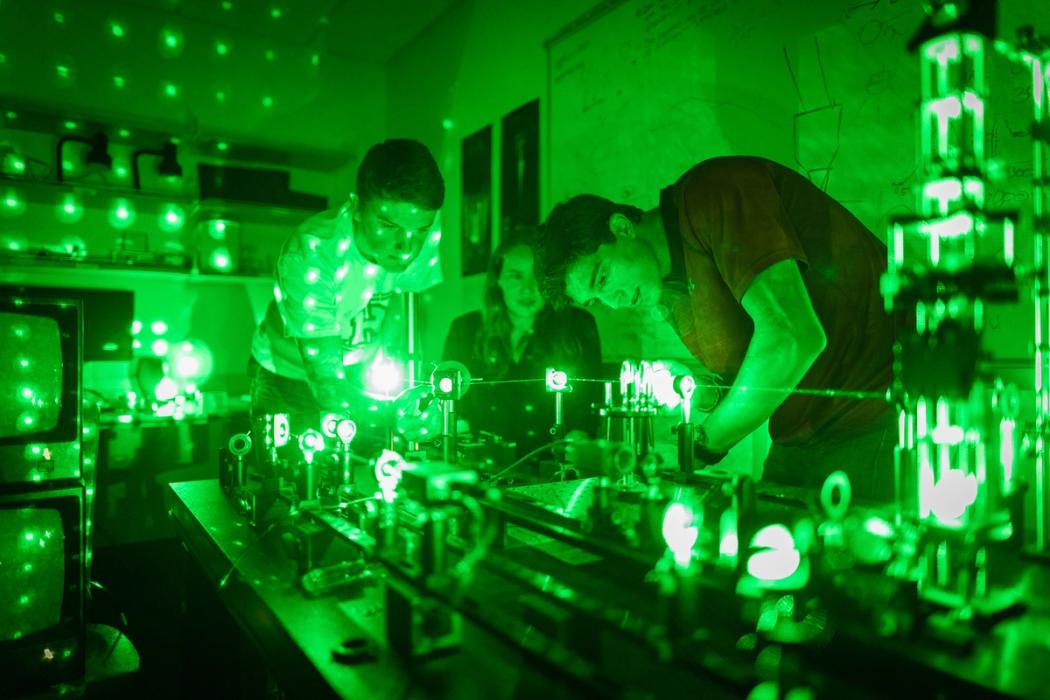 Green tinted photo with students working on lasers in physics lab.