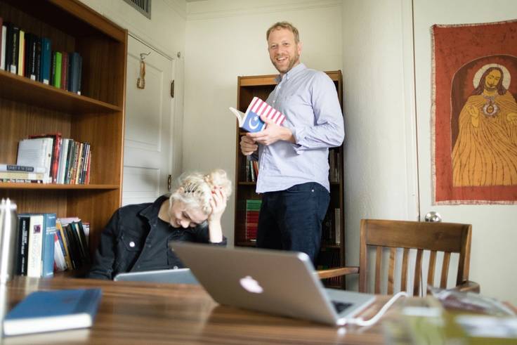 A religious studies professor stands with a book beside one of their students.