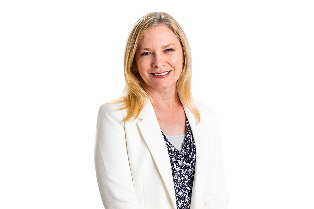 A smiling woman with blonde hair wearing a white blazer and a patterned top.