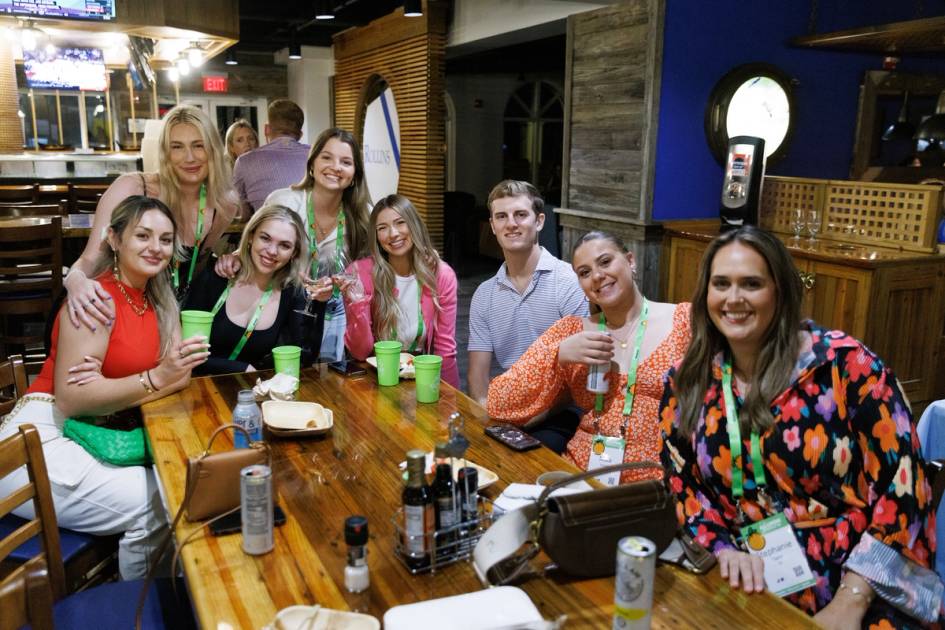 Gathering of alumni around a wooden table with food and drinks.