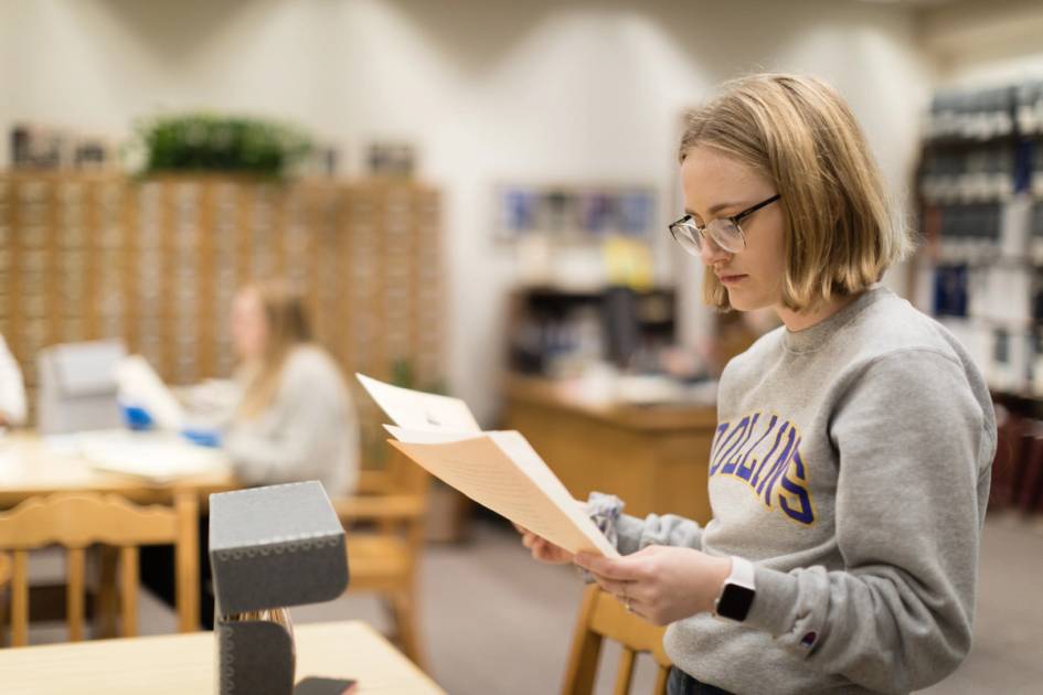 Student reading archival documents in a quiet library study area