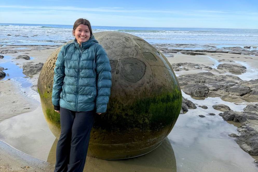 Sabrina Grace ’27 standing beside giant spherical boulder on a rocky beach.