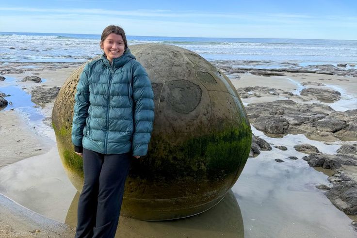 Sabrina Grace ’27 standing beside giant spherical boulder on a rocky beach.