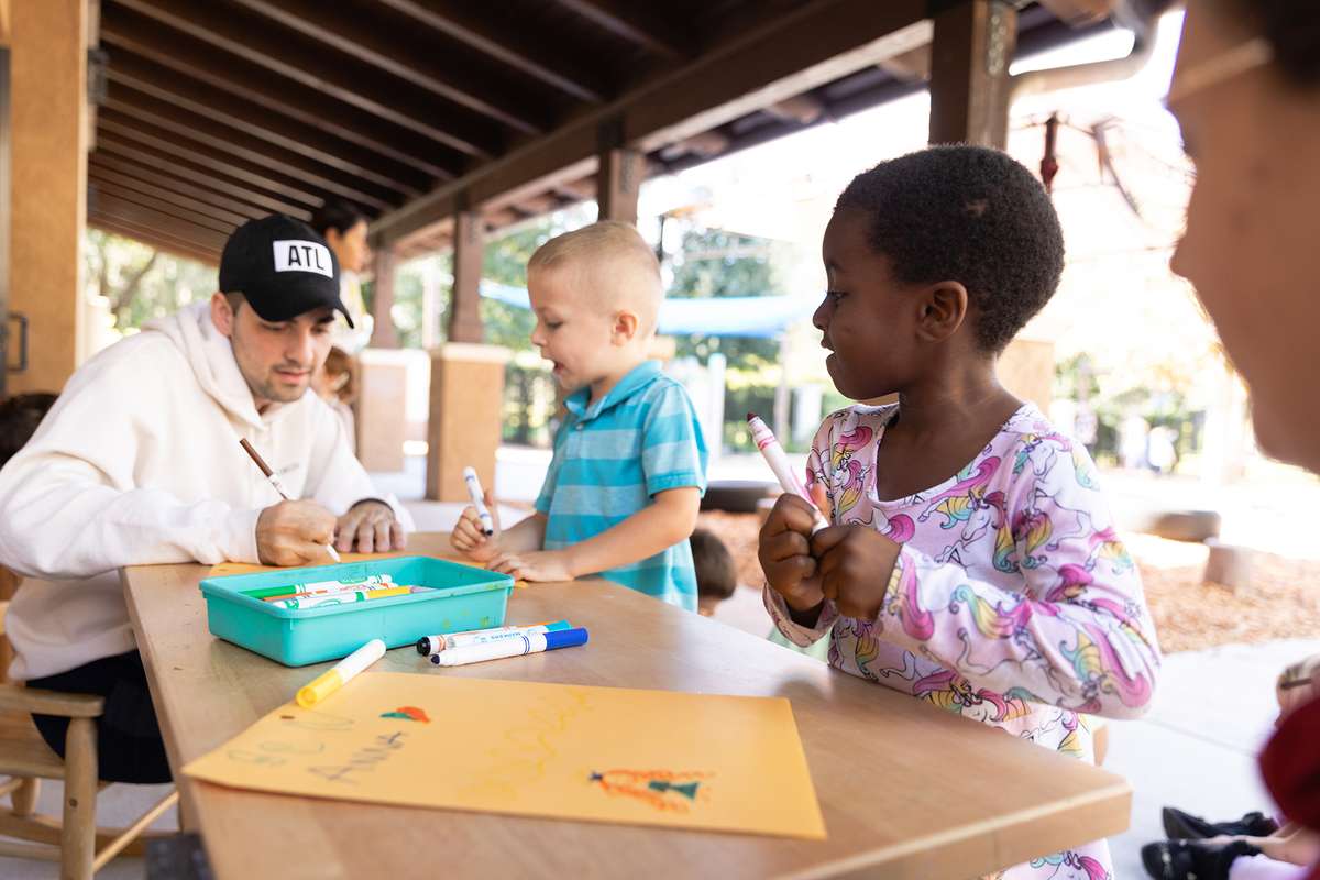 A college student coloring with children at an outside table at the child development center.