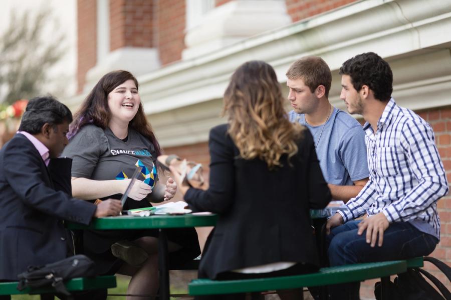 Professor Raja Singaram, Thais Cuachio with Deux Mains, and a group of students sitting outside at a table.