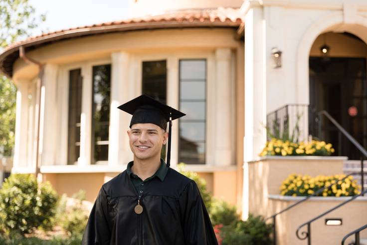 A college student poses in cap and gown before a commencement ceremony.