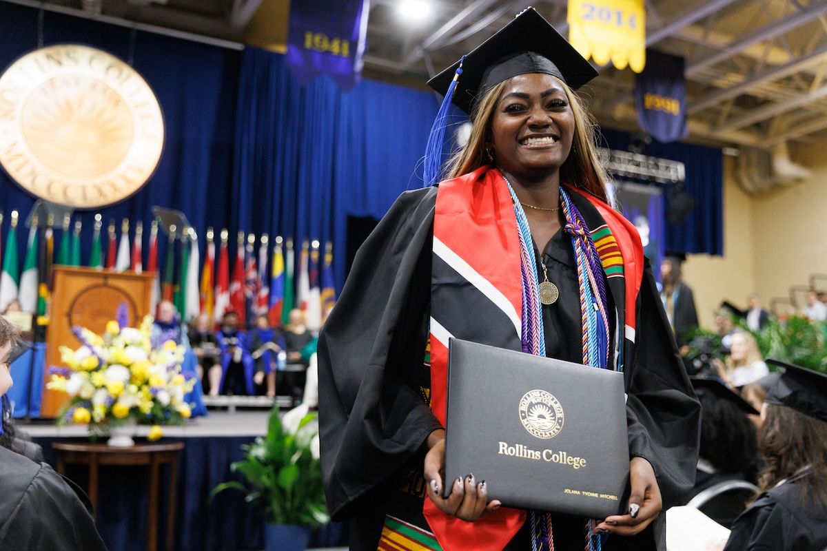 Student smiles at camera in cap and gown at commencement ceremony holding diploma