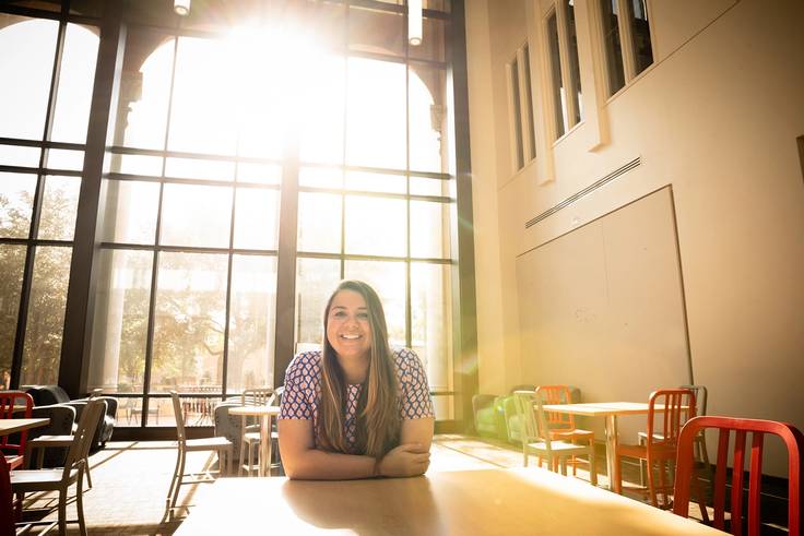 A student in a cap and gown poses in the Bush Science Center atrium.