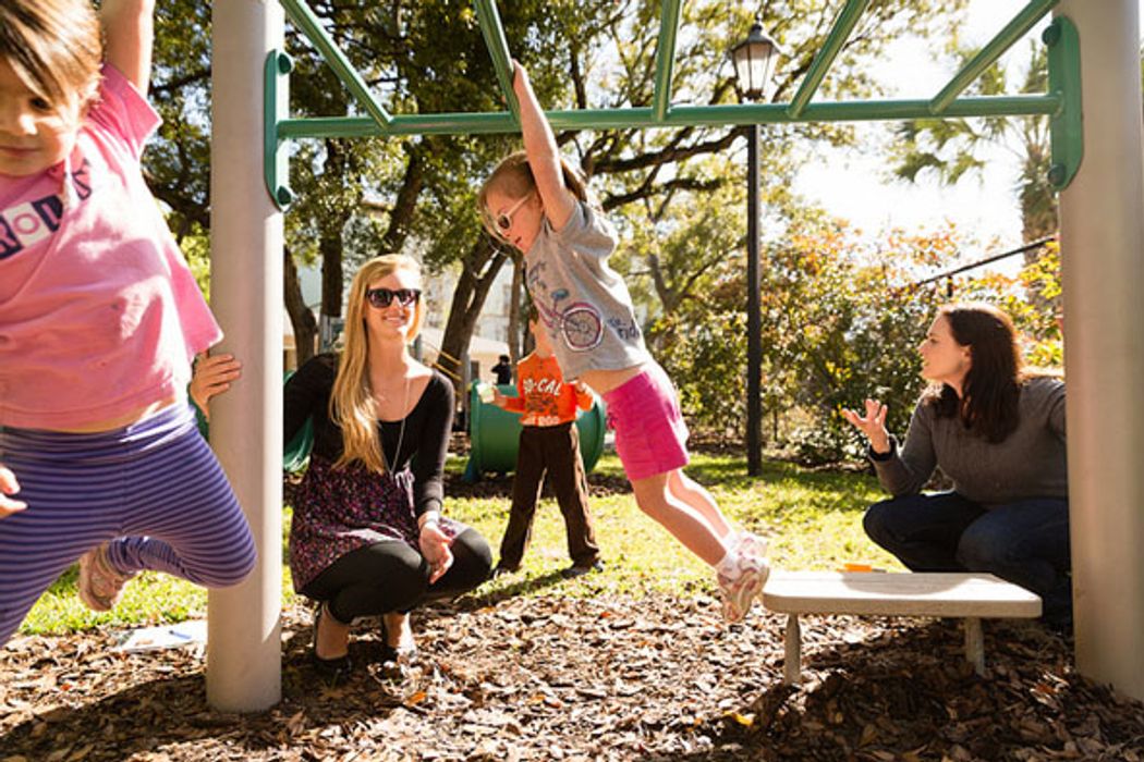 Preschool children play on a jungle gym with two teachers watching.