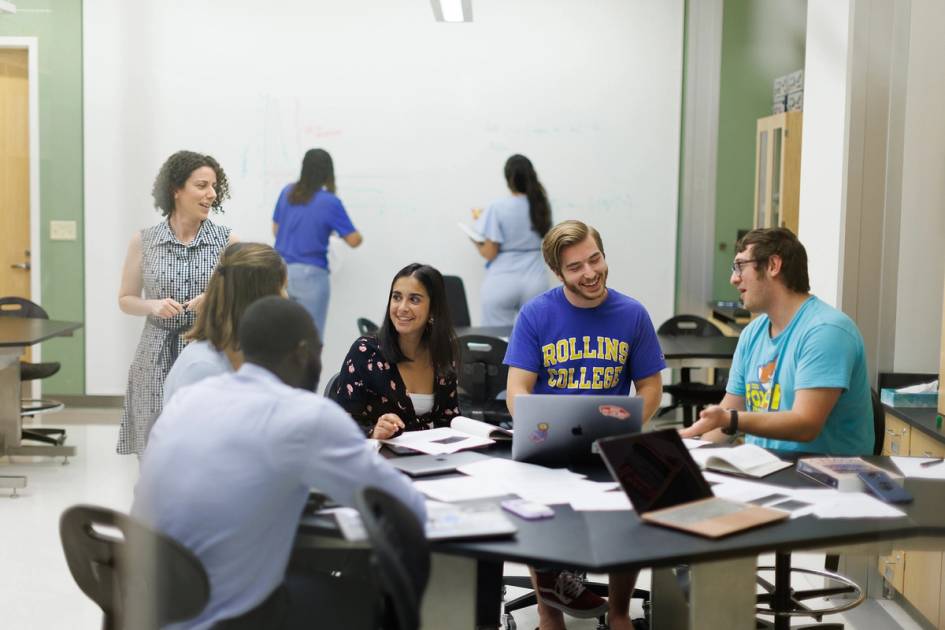 College students collaborate in an active classroom with laptops and whiteboards.