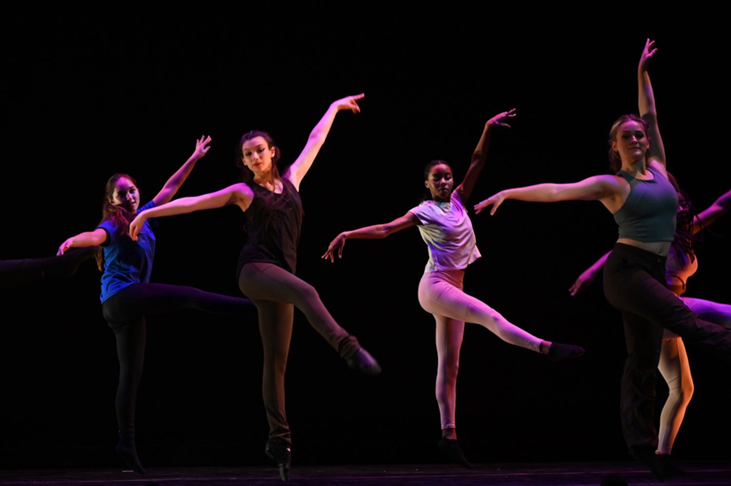 Four dancers in sync, arms outstretched and front leg in arabesque