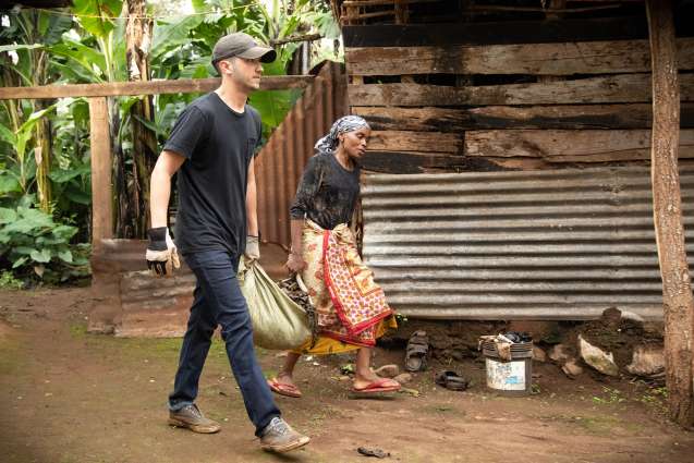 A college student helping a villager carry a heavy bag while on their class trip to Tanzania.