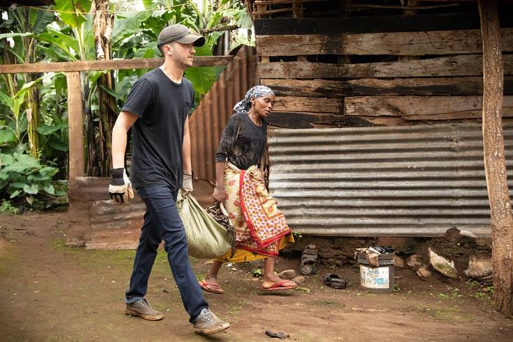A student helps a woman carry building materials in Tanzania.