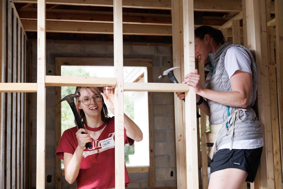 Two student volunteers nail studs into wall framing at Habitat for Humanity