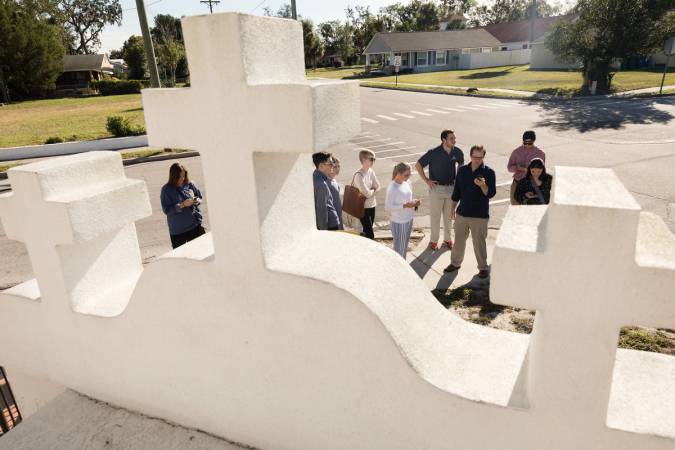 Students standing on a street corner behind three white crosses of a local church.