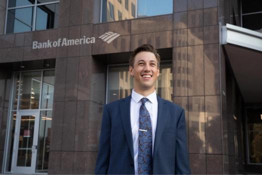 A recent college graduate poses in front of a Bank of America sign.