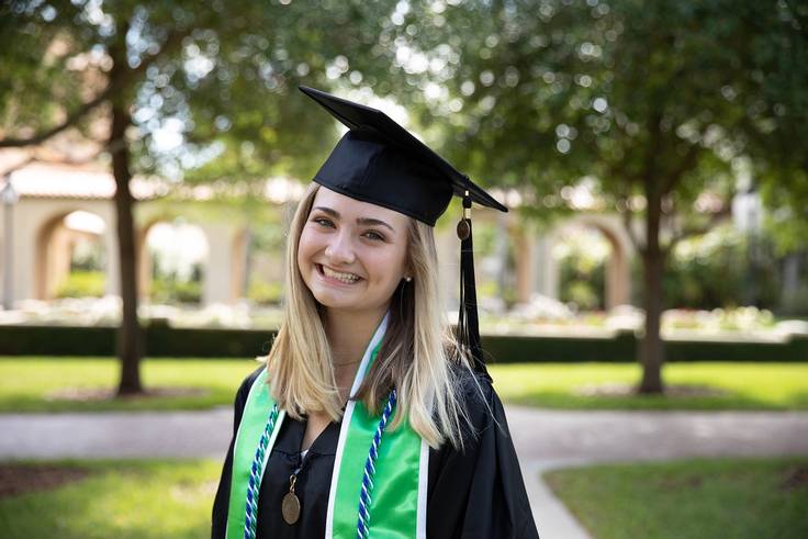 A student in a cap and gown poses on the Rollins College campus.