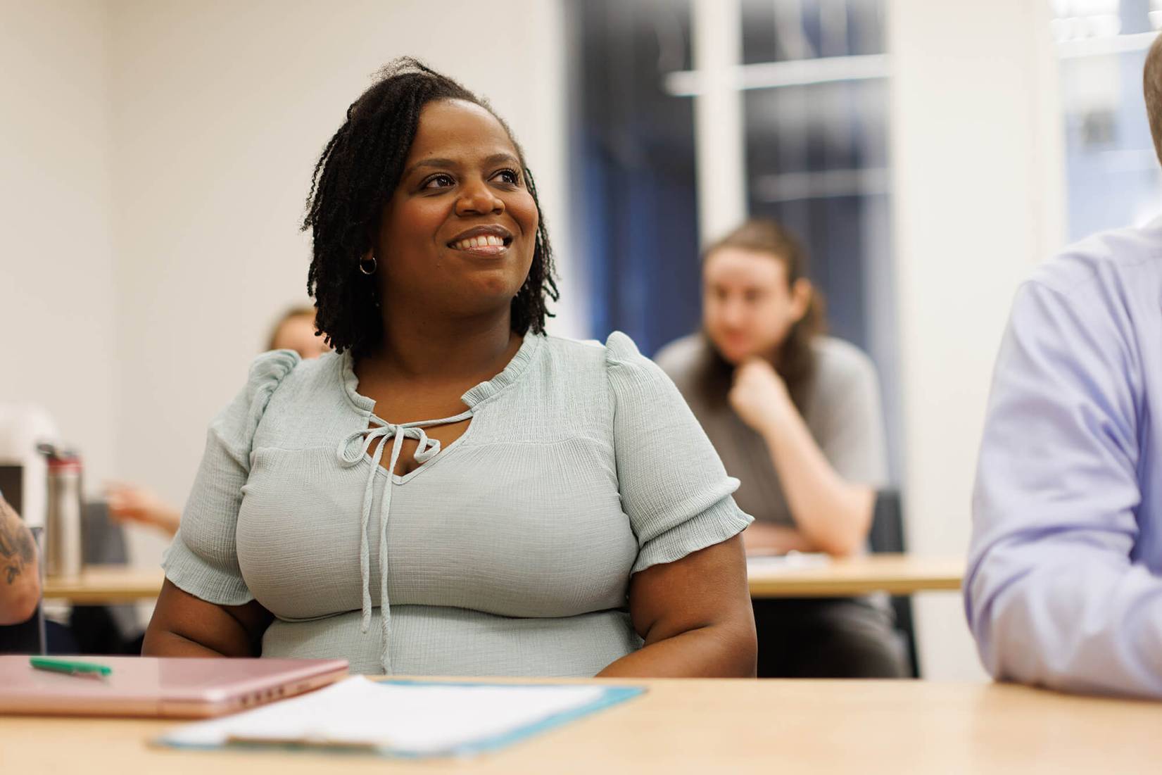 An adult college student smiles as she listens to a professor during class.