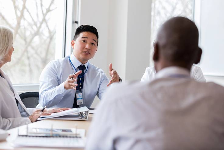 A public health professionals meets with a group of doctors.