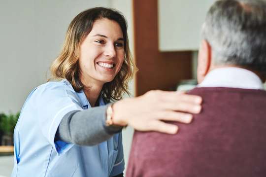 A public health worker places her hand on an elderly man's shoulder.