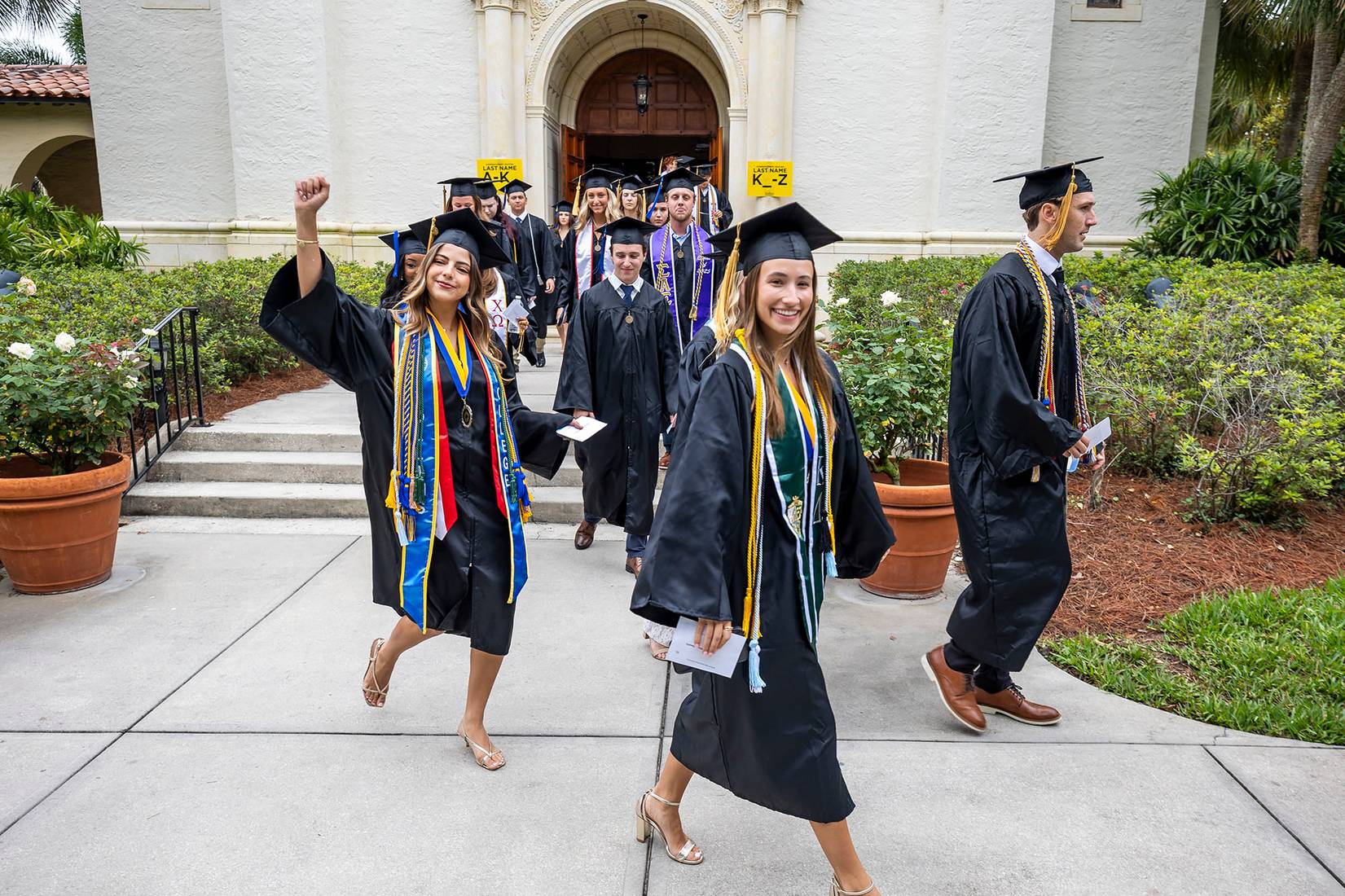 Rollins graduates in caps and gowns walking across campus during commencement procession.