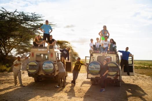 A group of college students pose for a photo on top of two safari jeeps.