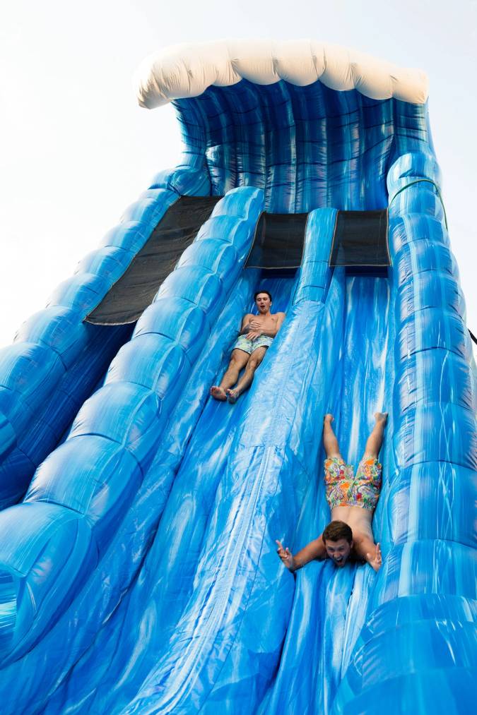 Two students slide down a blue inflatable slide.