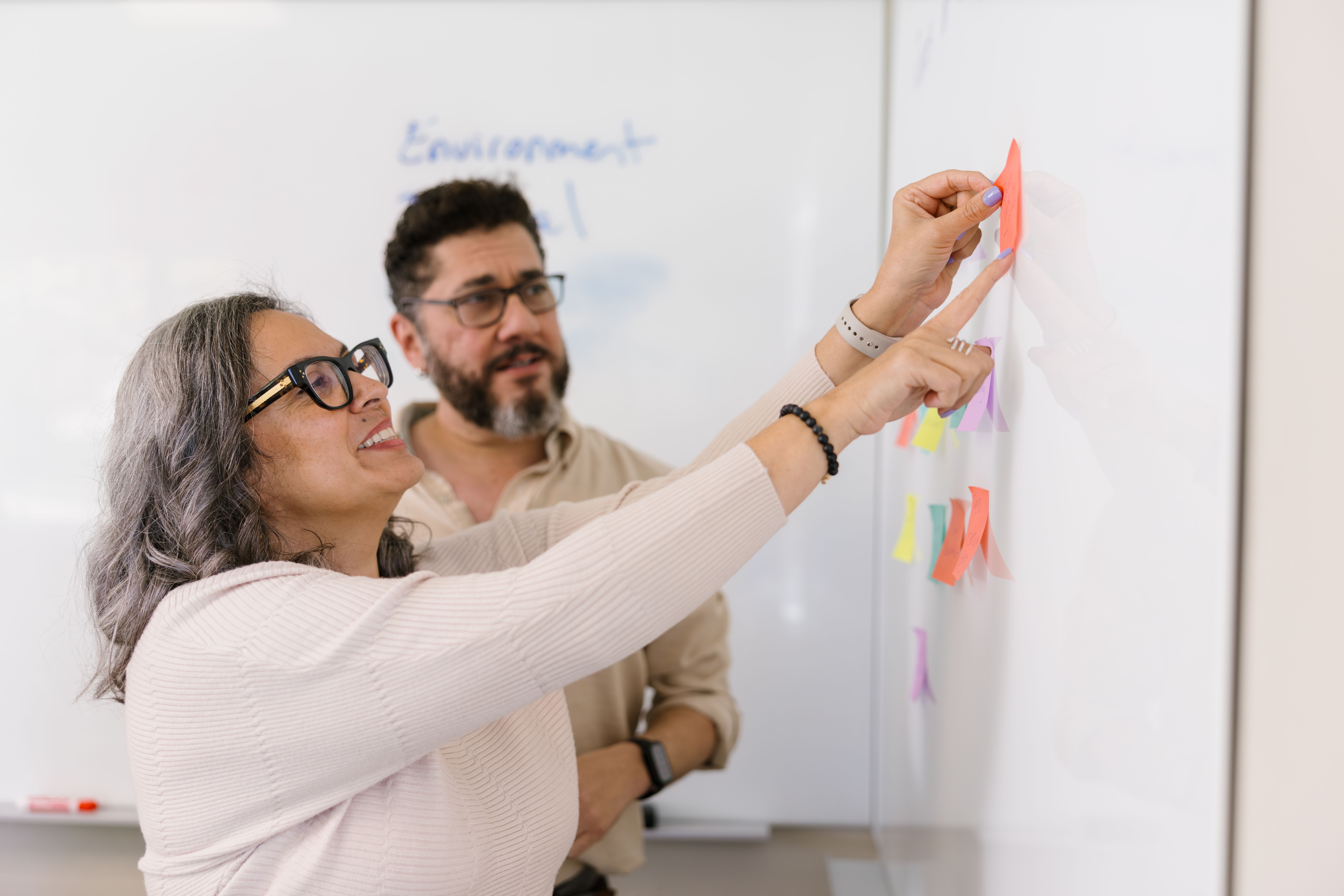 Two adults working on whiteboard. 