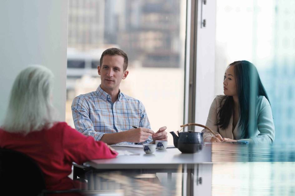 Colleagues in a meeting room discussing work around a conference table.