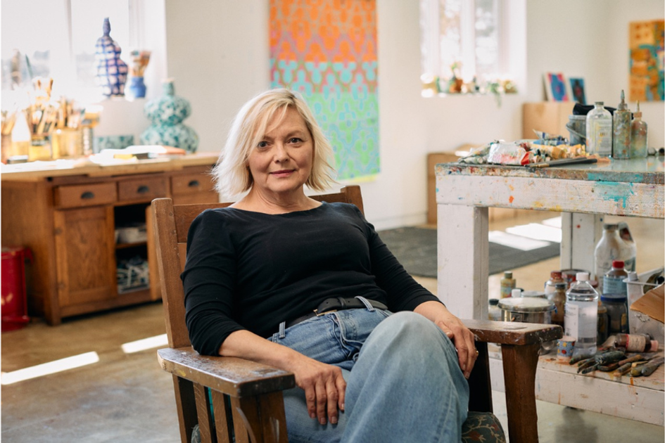 Artist  Judy Ledgerwood relaxing in a studio surrounded by paints, brushes, and canvases.