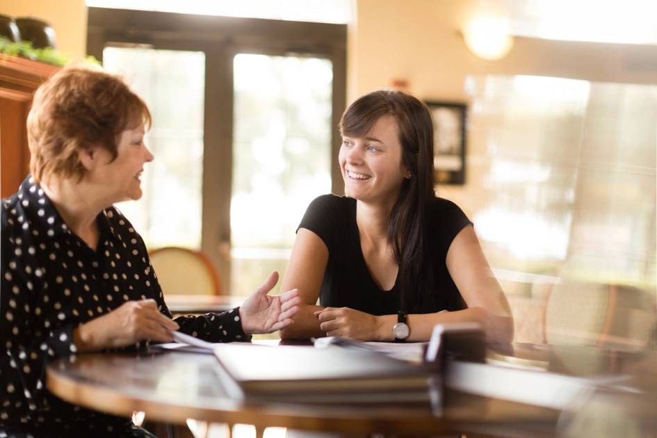 Two smiling women talking at a table.