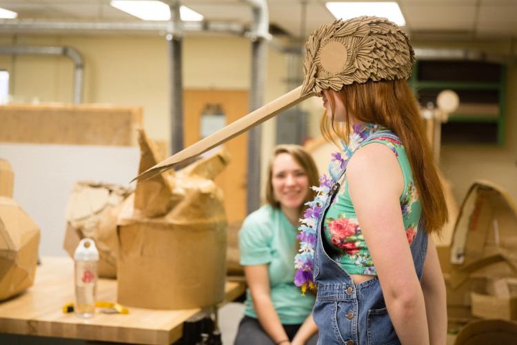 A student wearing a cardboard hummingbird hat that she made in her Foundations in Sculpture course.