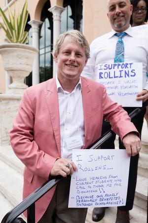 Rollins alumnus and donor holds a handwritten sign explaining why he supports Rollins.